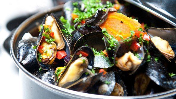 A bowl of mussels with tomatoes and parsley.