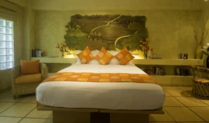 A bed with orange pillows and a green painting on the wall.